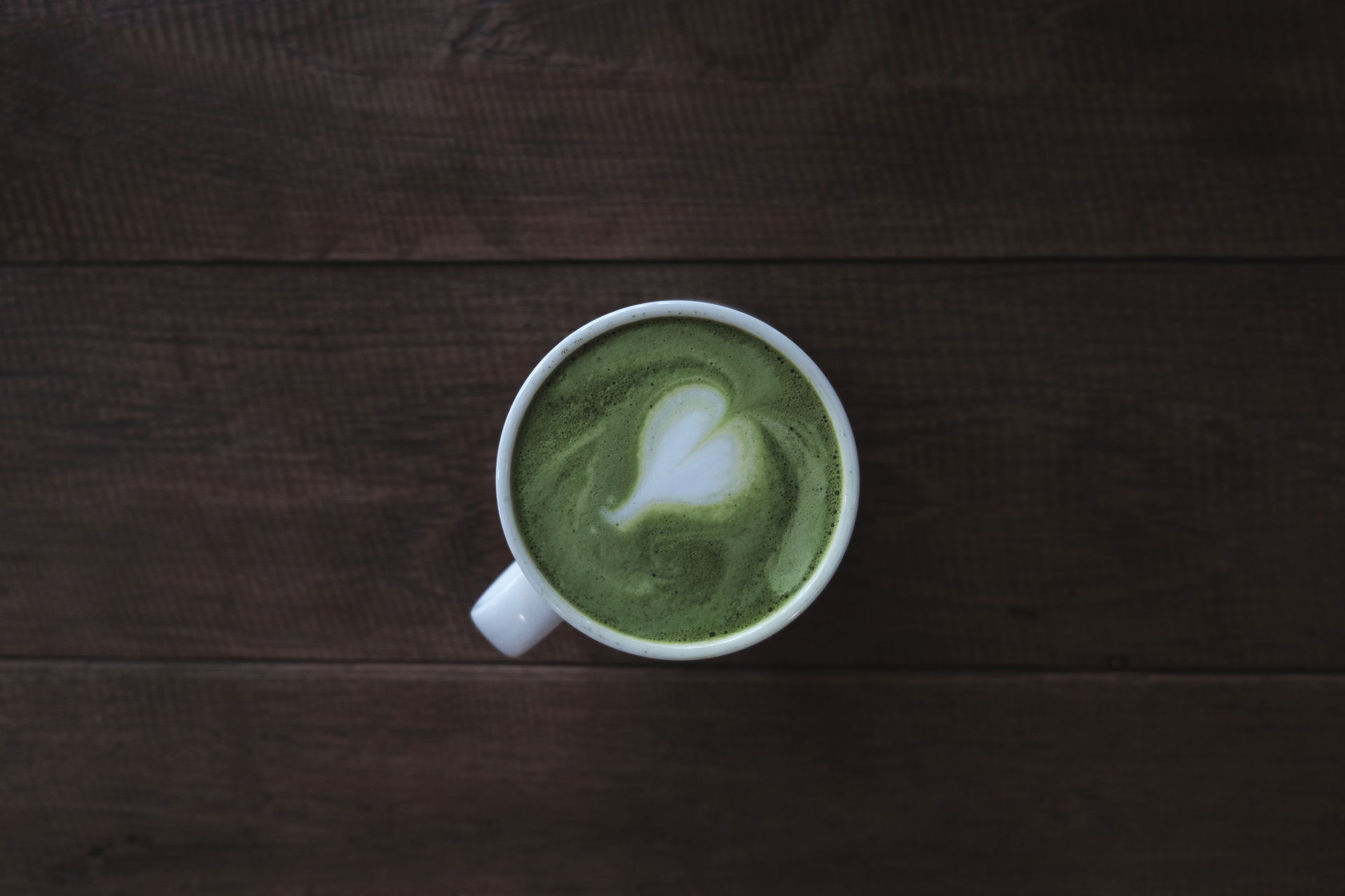 A white mug of matcha green tea with a heart made in latte art …