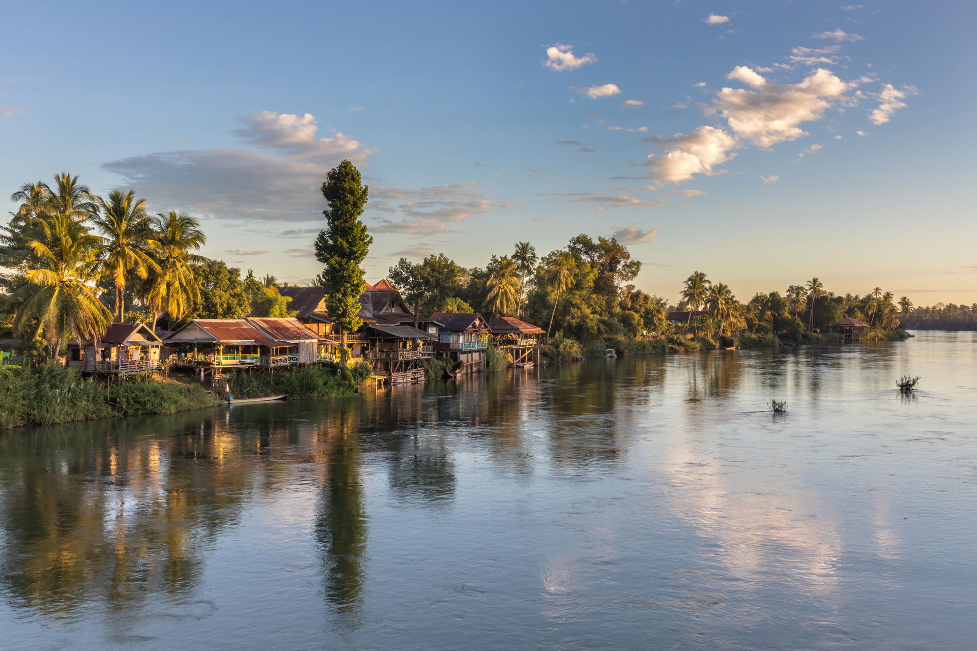 Mekong bank with stilt dwellings, trees and clouds at golden ho…