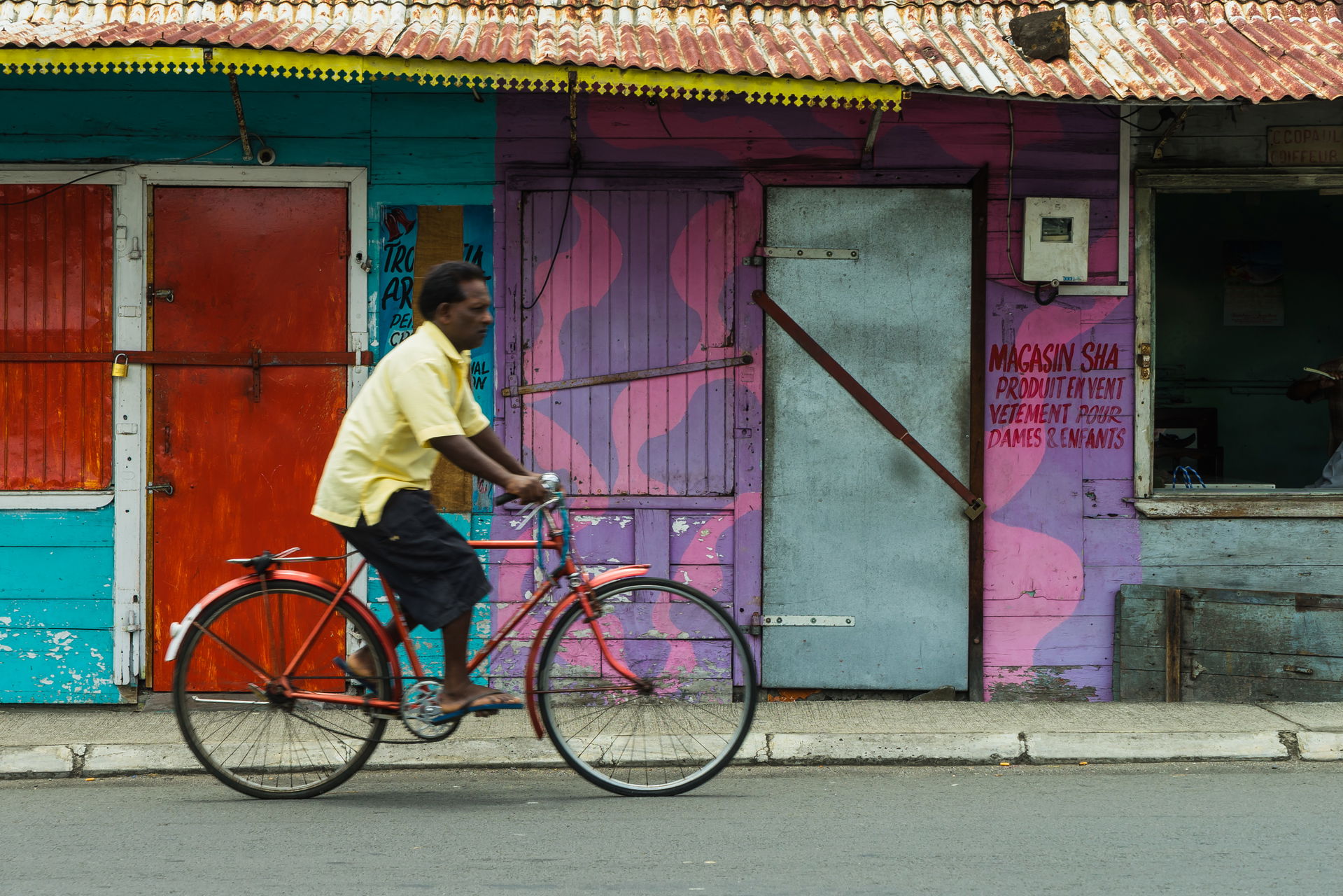 A man rides his bicycle in front of some colorful storefronts i…