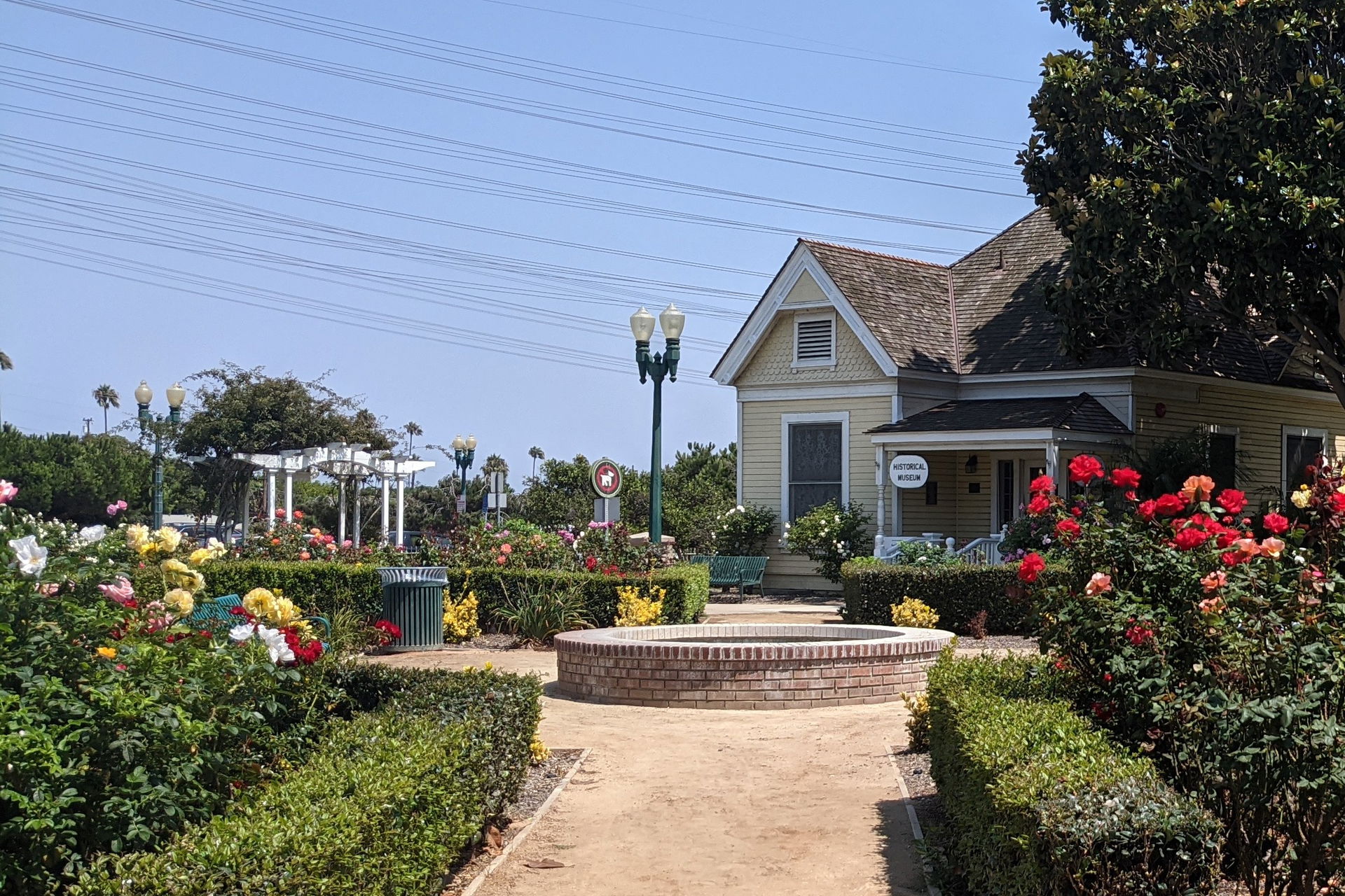 A dirt path through a rose garden to a dry fountain, an old hou…