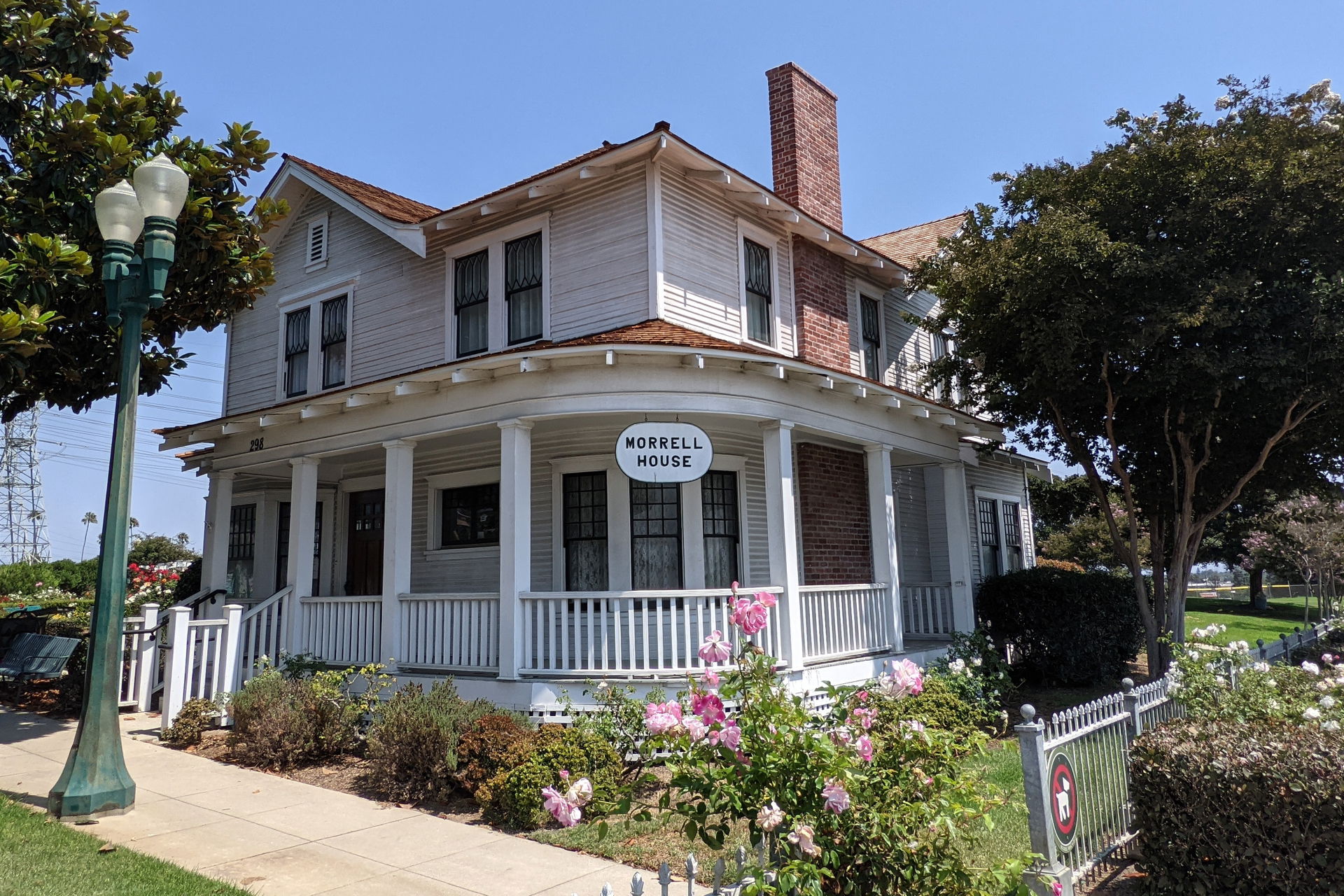 A two story white-painted wooden house with wraparound porch, w…