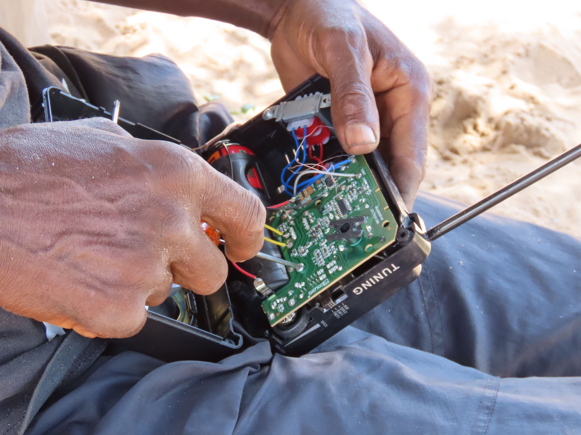 The picture depicts a man fixing a radio at Onekwaya East Villa…