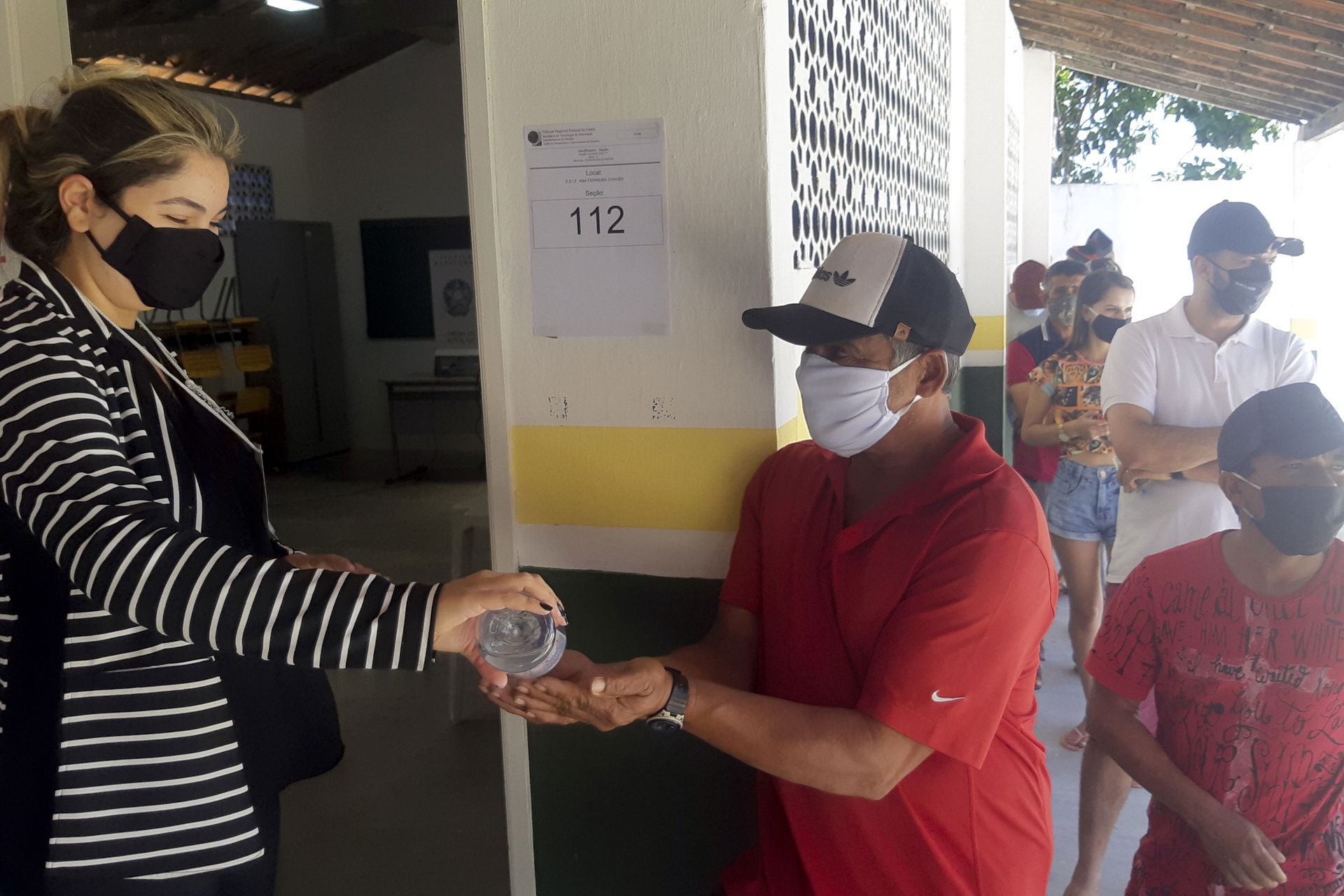 Mesária coloca álcool gel nas mãos de eleitor antes de votar.
F…