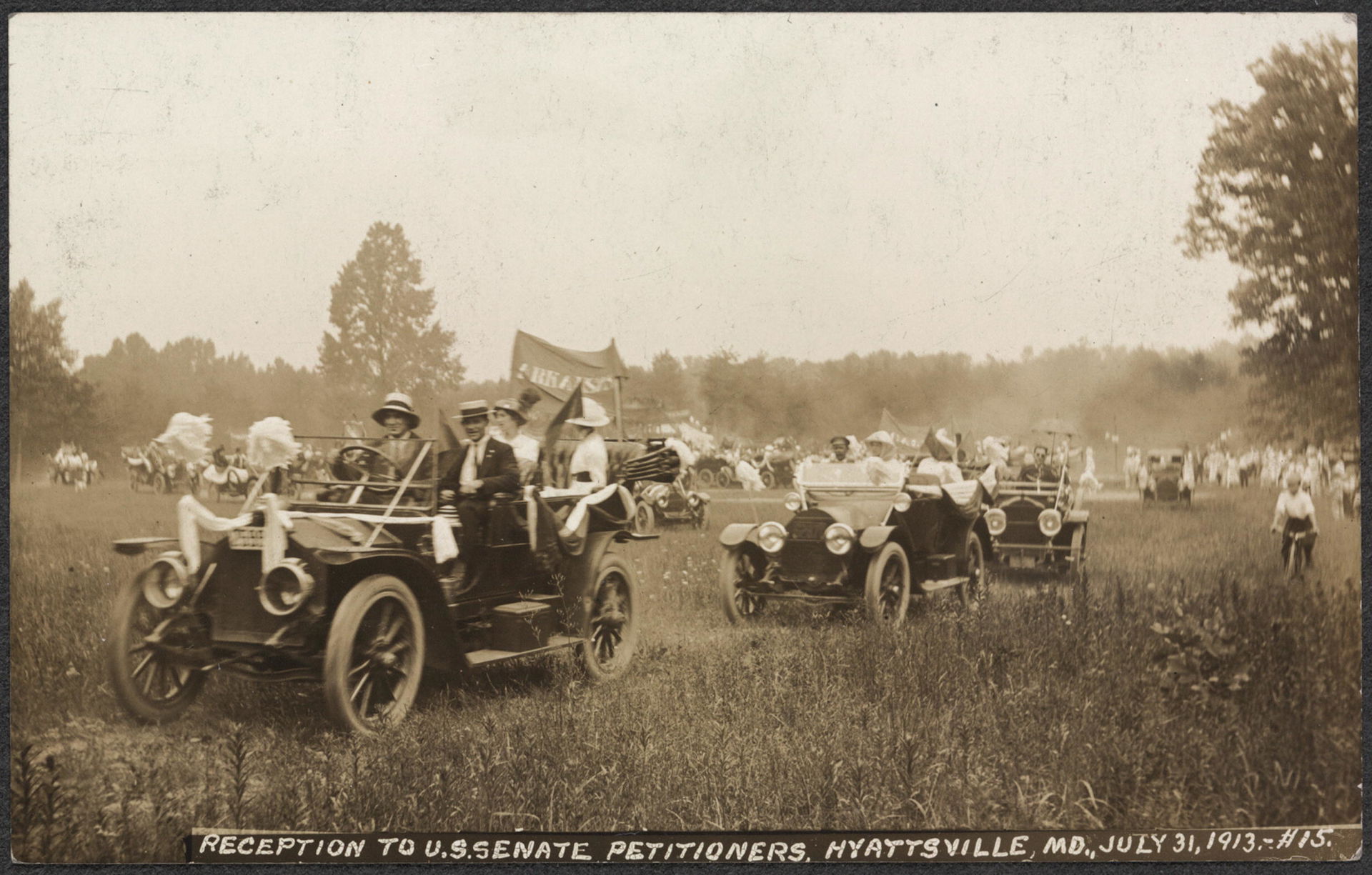 Summary: Postcard image of people driving cars, tops-down, thro…