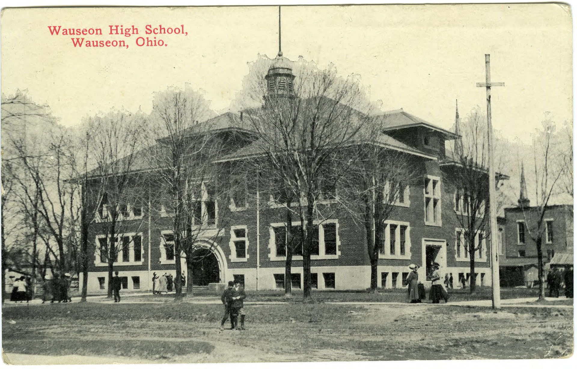 Black and white photograph of a brick school building with peop…