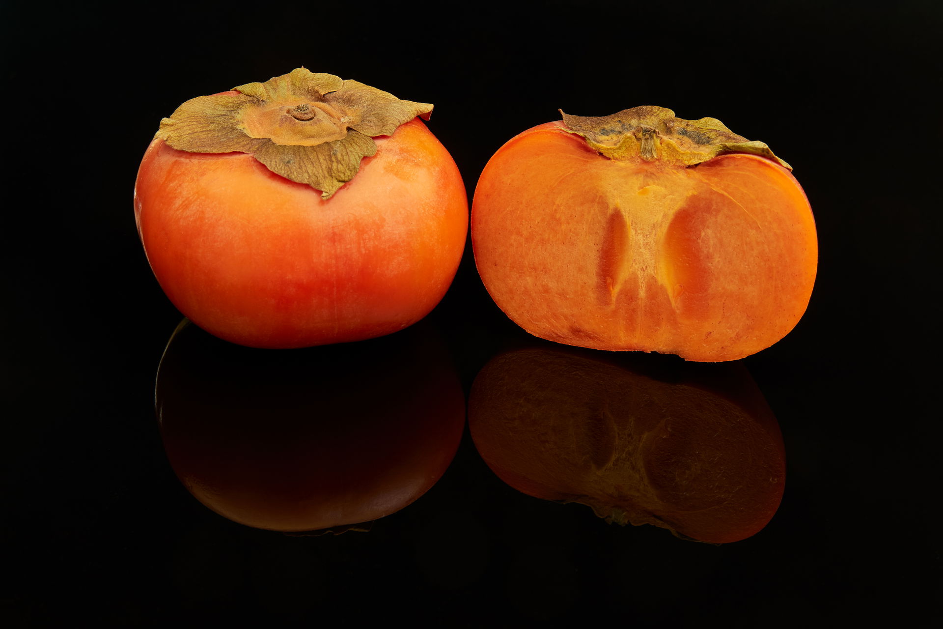 Two fuyu persimmon fruits (Diospyros kaki), one cut in half