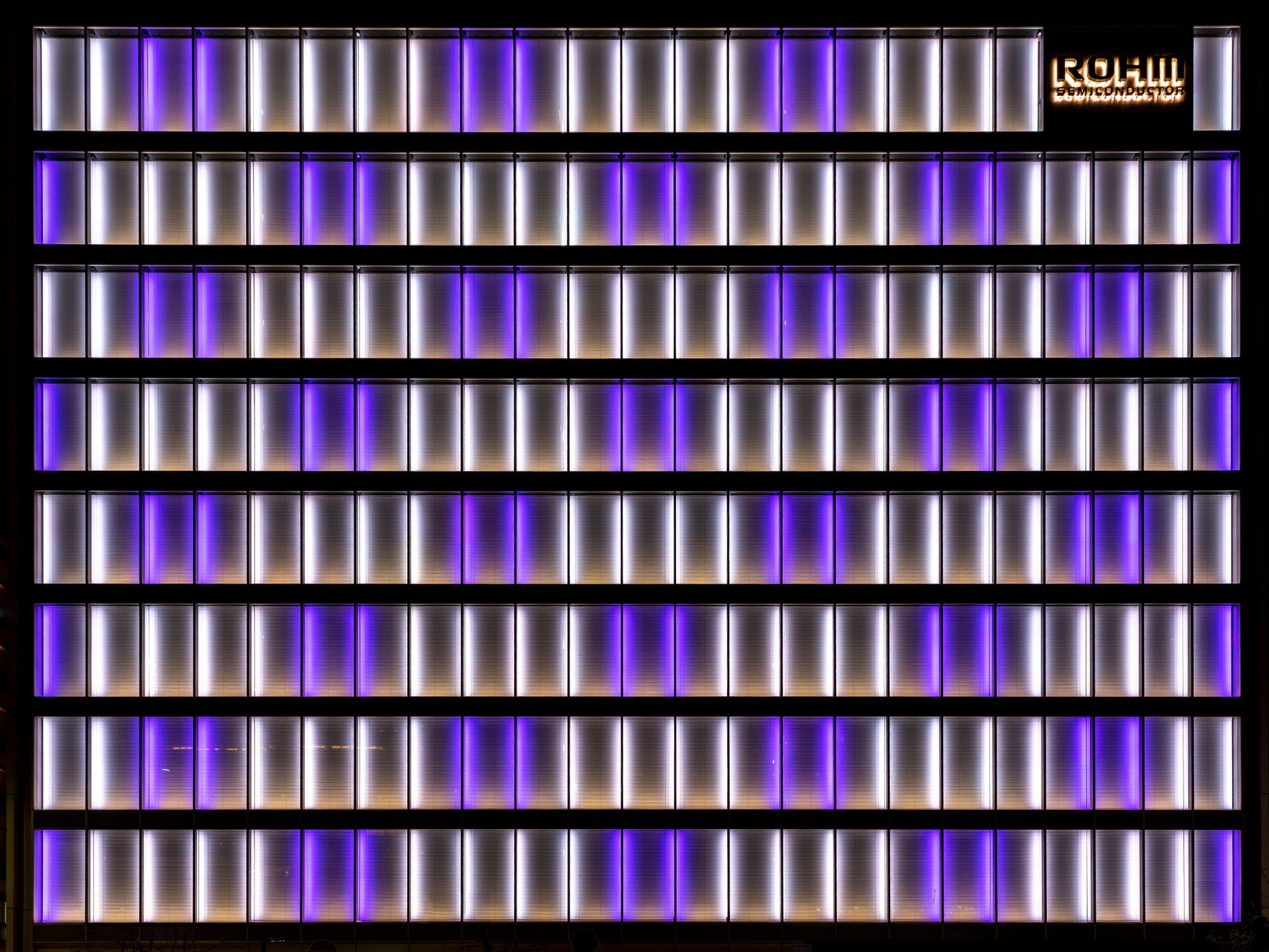 The illuminated white and purple facade of the office building …