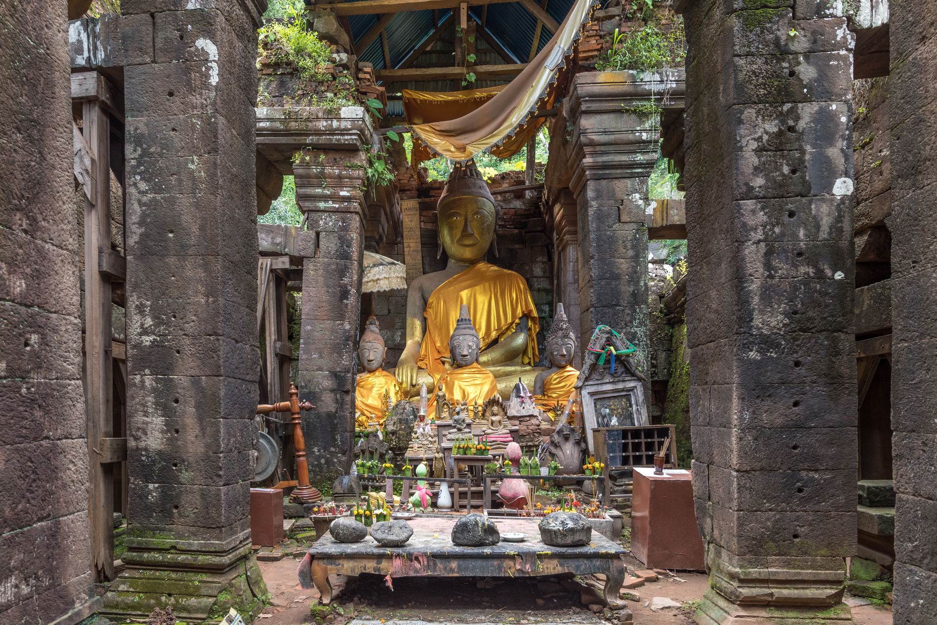 Clothed statues of the Buddha seated, table with stones and Bud…