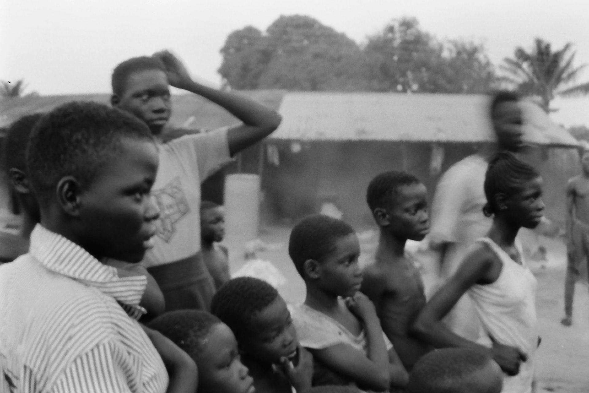 This black-and-white photograph shows a group of children gathe…