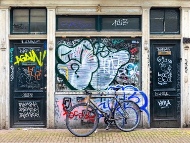 Bicycle parked in front of a graffitied building façade with do…
