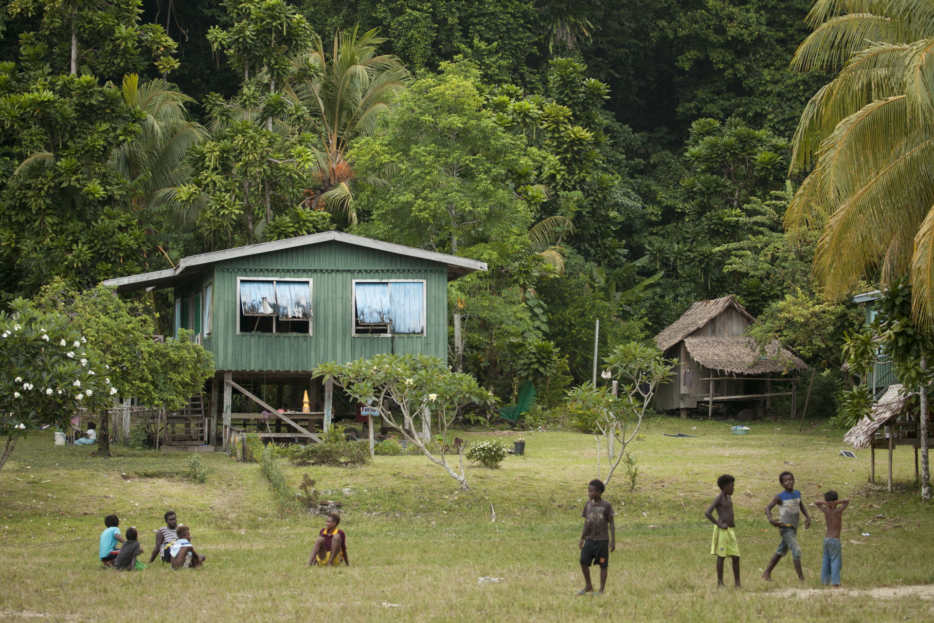 People interact on a large open field outside the schoolhouse. …